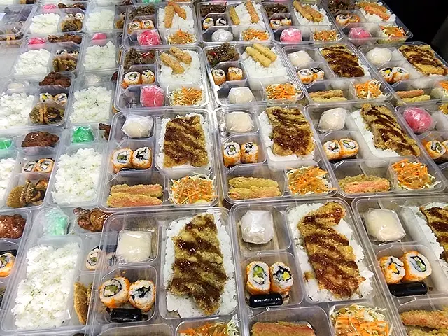 Rows of packed meals with rice, sushi rolls and viands